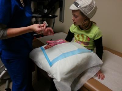 photo of a child in a clinic, in the process of having a pink arm cast removed by a physician