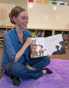 a person sits on a purple rug, holding an open children's book