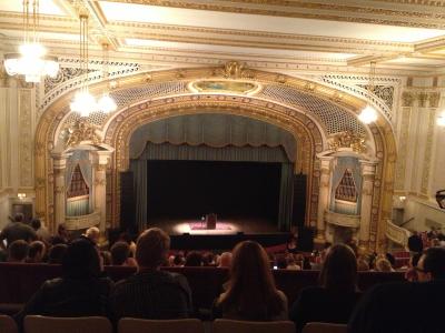 view of an empty stage in a crowded theater, and a spotlight showing a lectern, stool, and a microphone