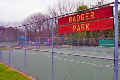 sign reading "Badger Park" on fence around tennis courts