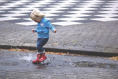 photo of child splashing in a rain puddle on a street