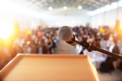 photo of a microphone and lectern in front of a waiting audience
