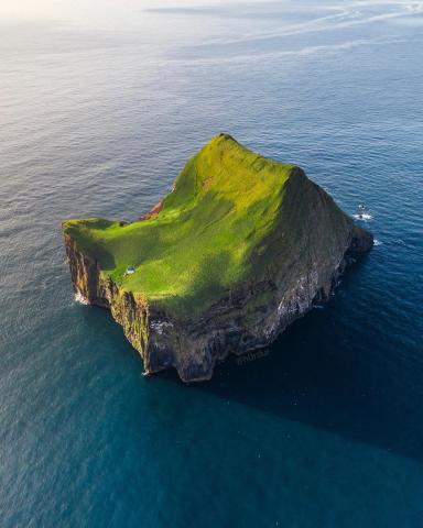 photo of a tall, rocky, bare island, with a single small house on it, surrounded by the ocean.