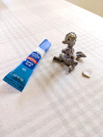 photo of a small, ceramic dragon with a broken wing, next to a tube of super glue