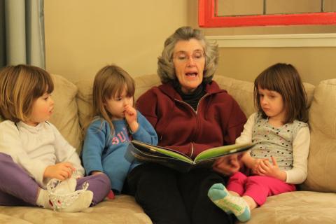 photo of a grandma reading a story to three young children, seated together on a couch