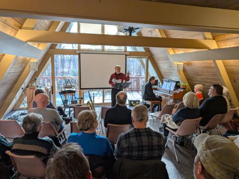 a group of people in an a-frame with a speaker in a red shirt and someone else at a piano