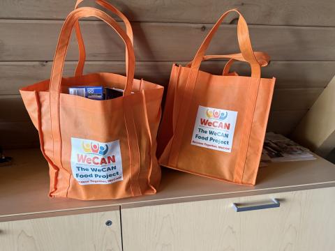 photo of two orange grocery bags with the WeCAN logo and the next "The WeCAN Neighborhood Food Project" on them.