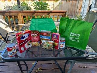 green grocery bags and non-perishable food items to donate, arranged on a table