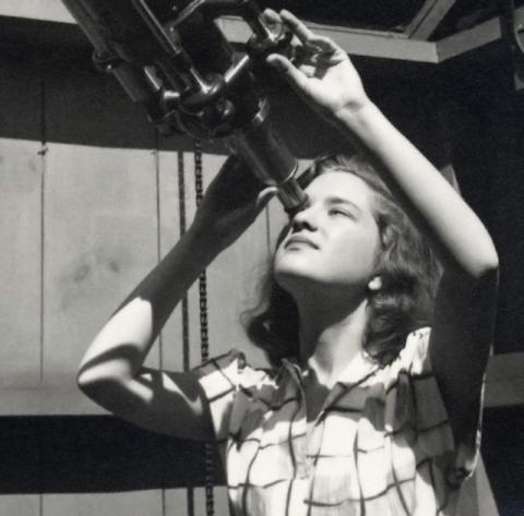 A young Vera Rubin looking into the eyepiece of a telescope