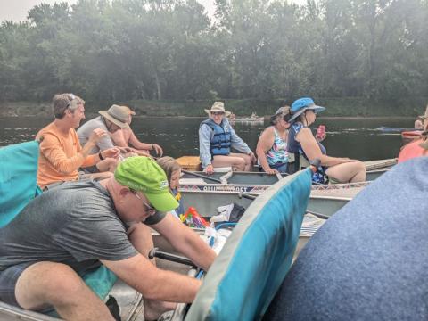 several people of varying ages in canoes on a wooded river