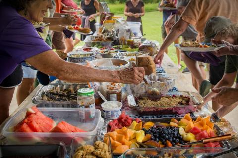 people helping themselves to food at a summer picnic potluck
